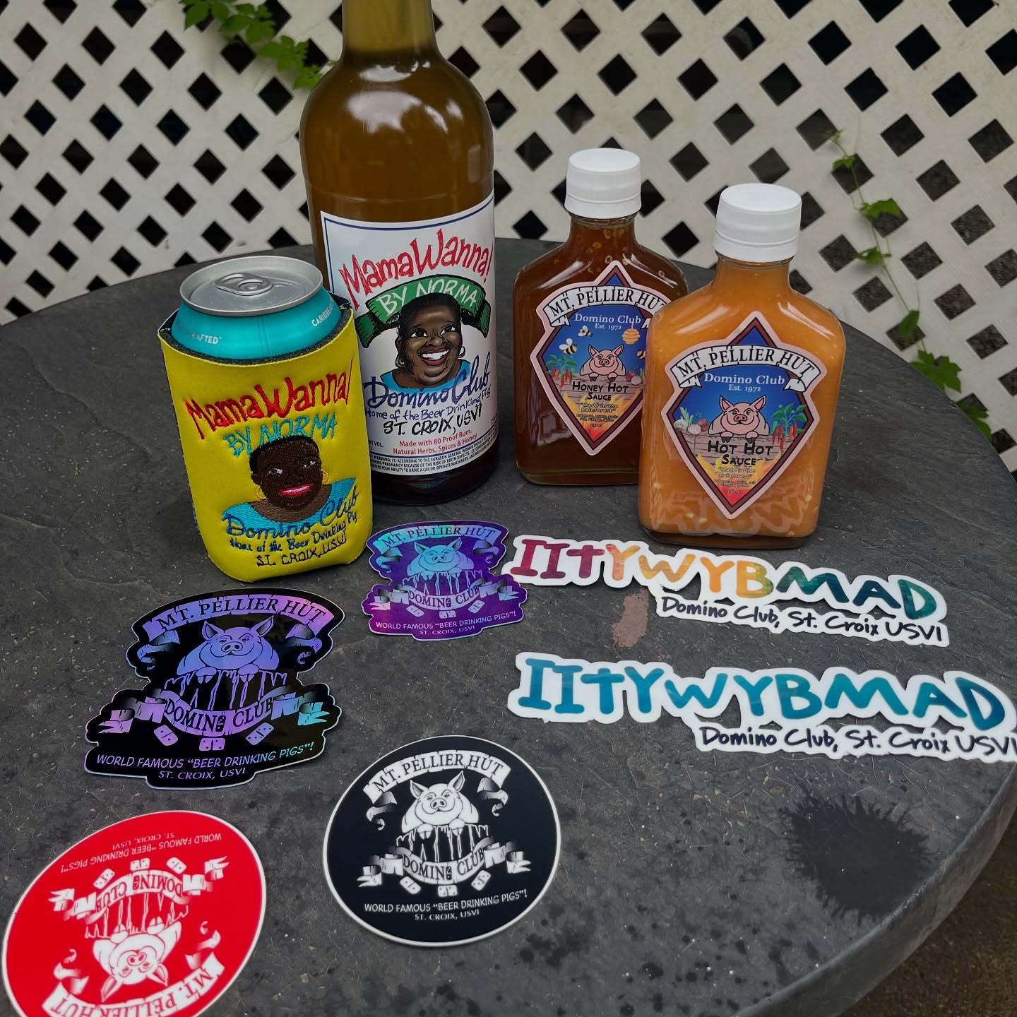 MamaWanna bottle, beer koozie, Mt. Pellier Hut hot sauces, Domino Club stickers, and IITYWYBMAD bumper stickers on display