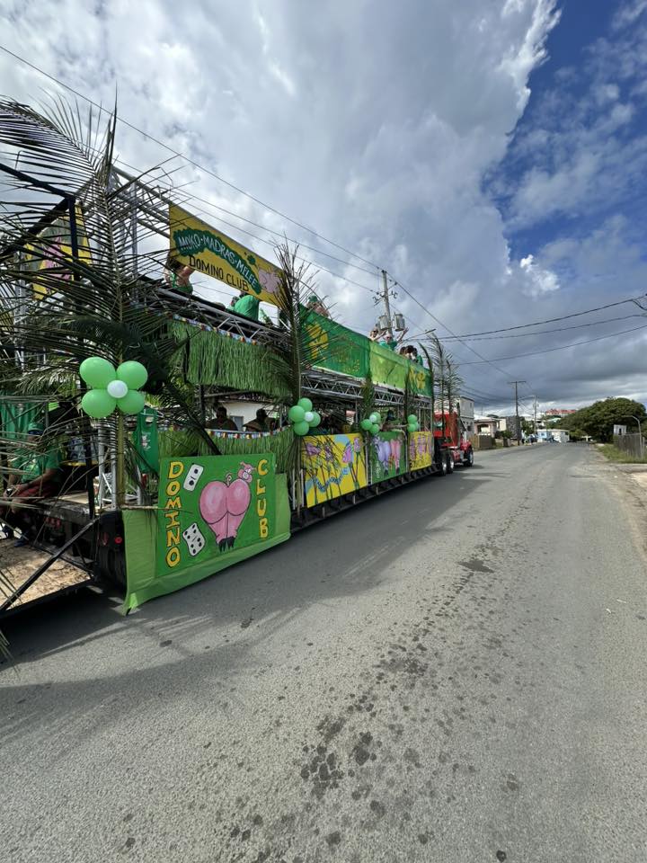 The massive Domino Club St. Patrick's Day parade float decorated in green with balloons, pig artwork panels, and domino imagery rolling through Christiansted