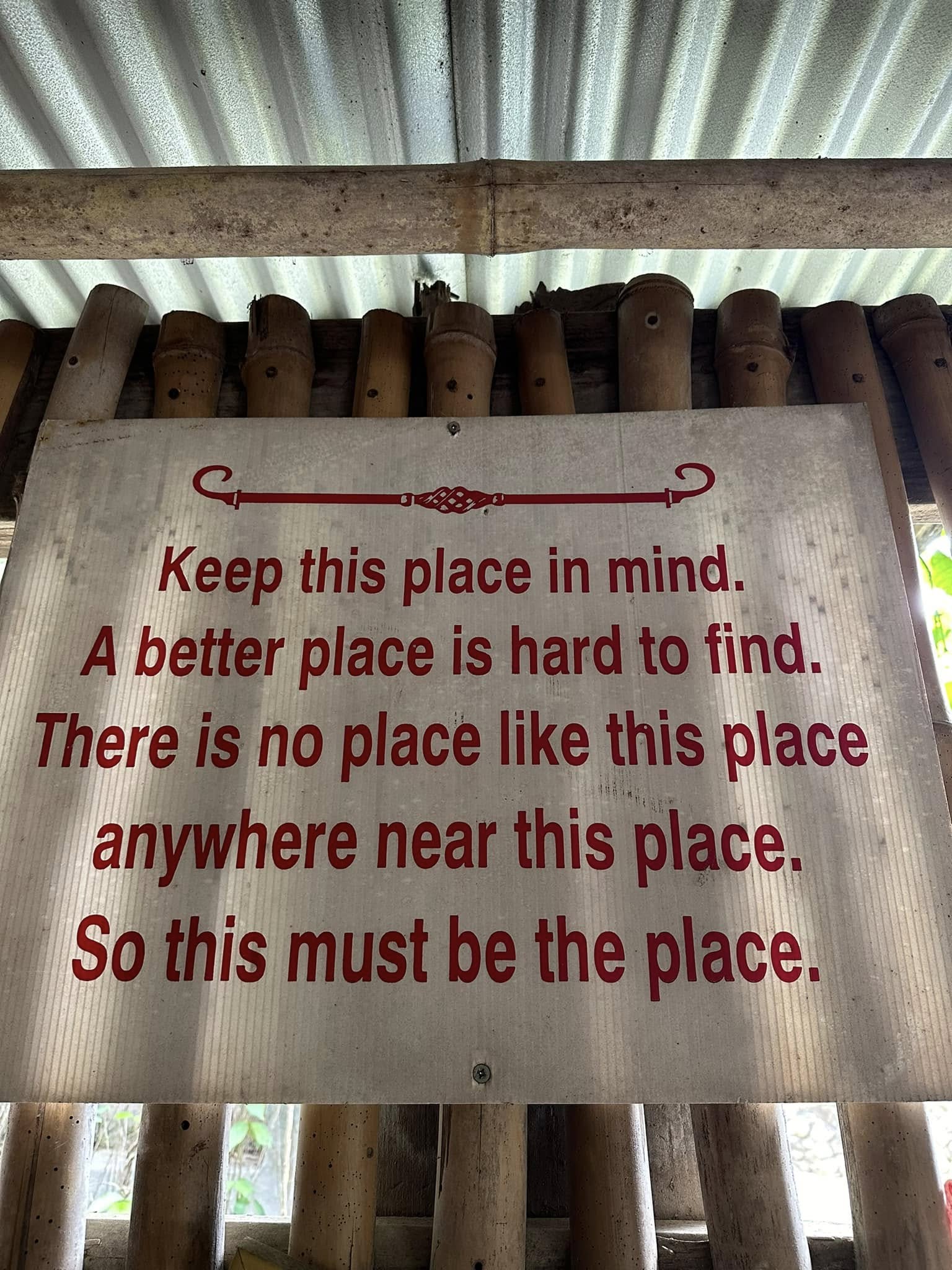 A hand-lettered poem on white sign reading 'this must be the place' on the bar's bamboo wall