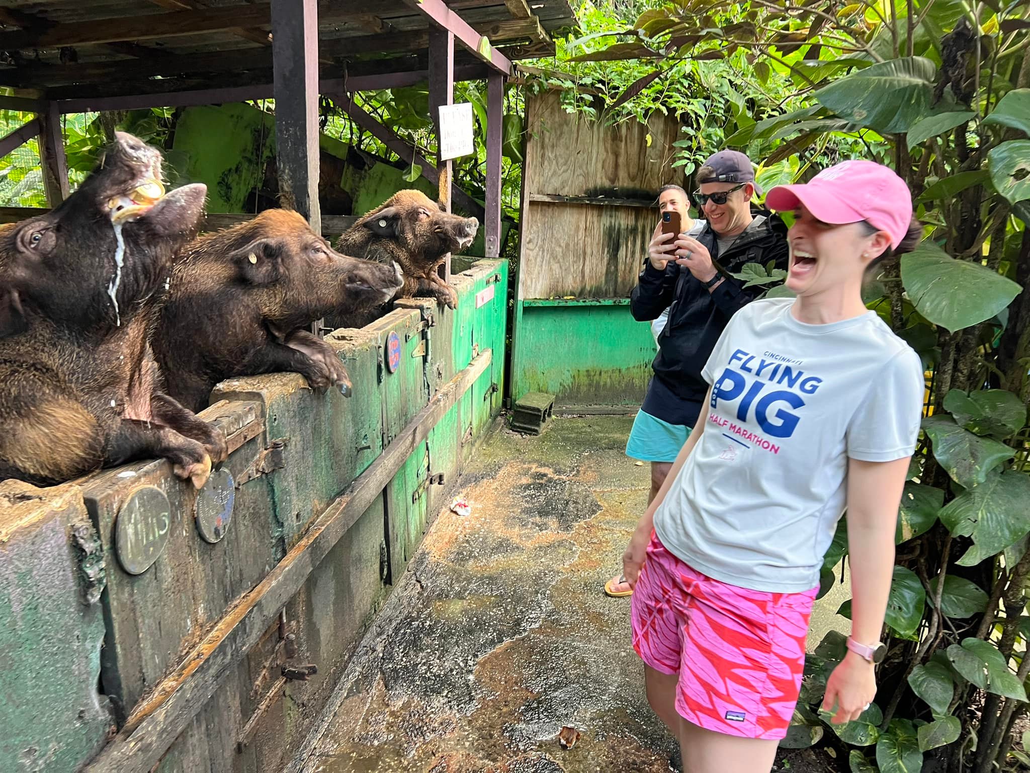 Excited visitors interacting with pigs at the fence, one wearing a Flying Pig t-shirt